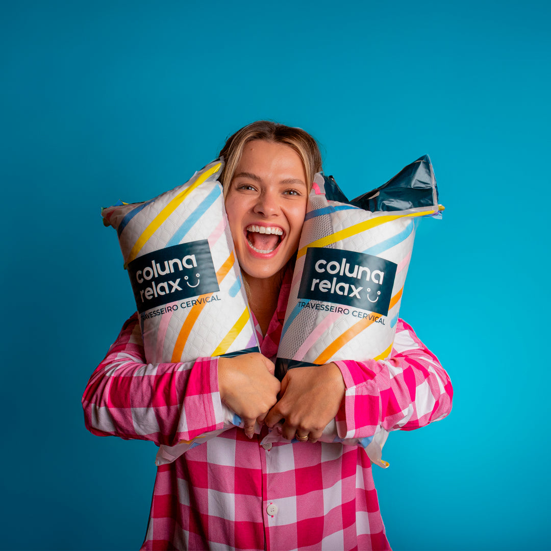 Happy model holding two packages of the cervical pillow Coluna Relax with her pink and white I wanna sleep pajamas